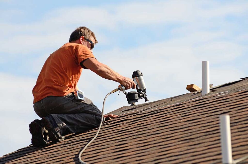 A homeowner examining damaged shingles and moss growth on a sloped asphalt shingle roof.
