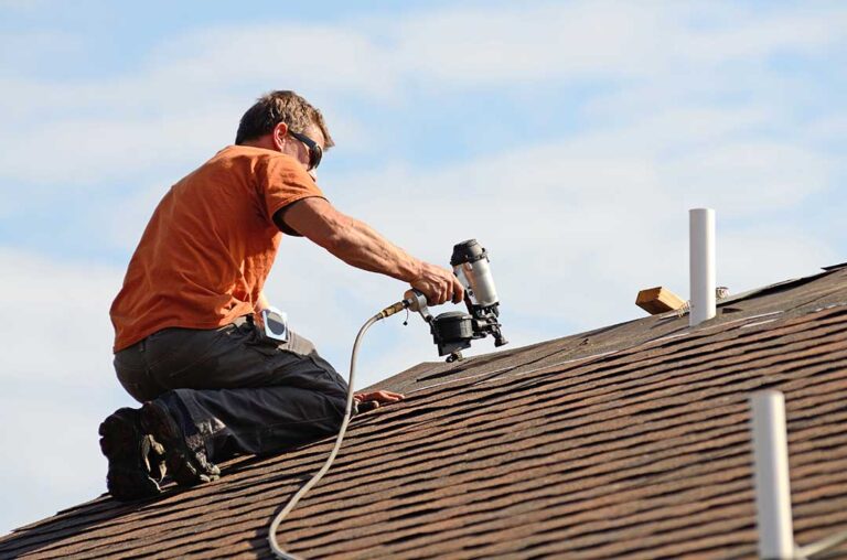 A homeowner examining damaged shingles and moss growth on a sloped asphalt shingle roof.