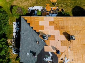 A homeowner examining dark streaks and green patches on grey rooftop shingles during daylight.